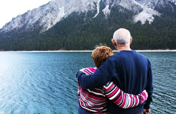 Photo of older couple looking out over water and mountain. 